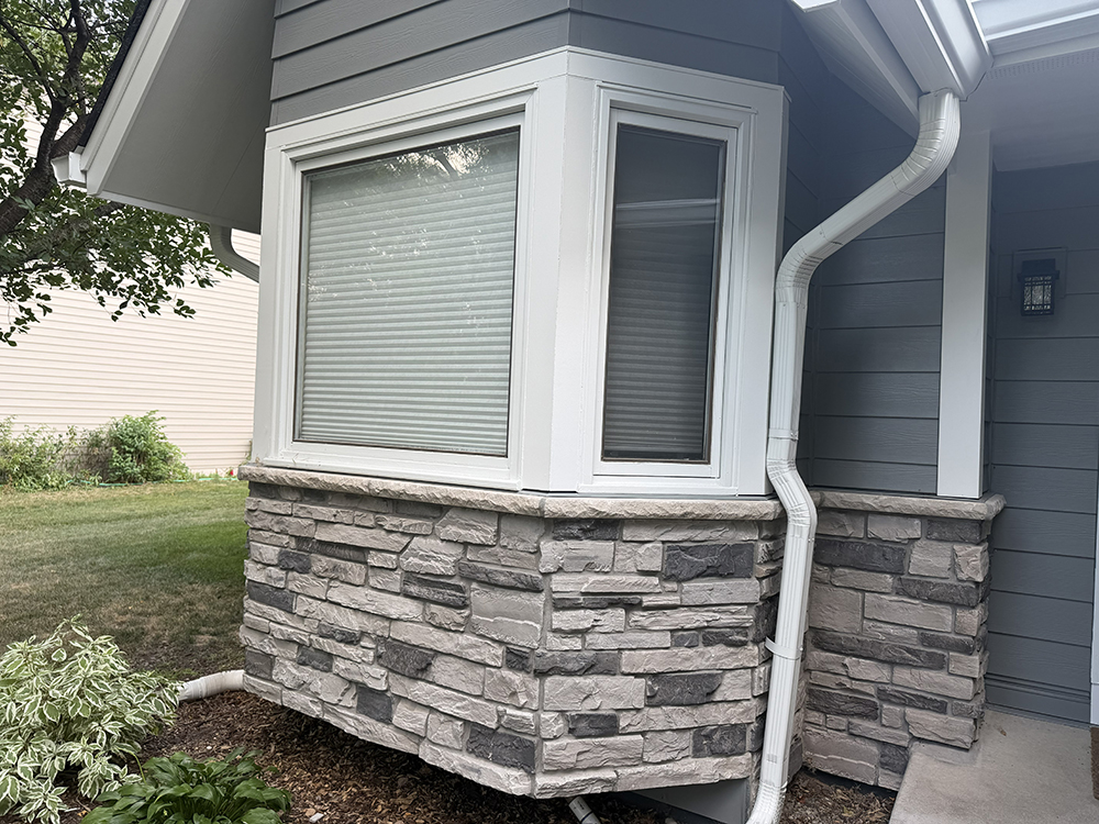 Gray siding with white trim and stone around bay window on Maple Grove home